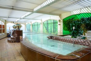 A large indoor swimming pool with a curved edge, a seating area with a table and chairs, and a green wall with plants. - Hotel Listel Inawashiro Main (Inawashiro)