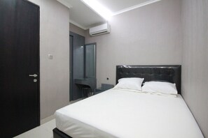 A bedroom with a bed, a dark door, a mirror, and an air conditioning unit. - Harvia Suites (Jakarta)