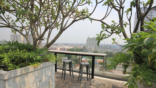 A balcony with a view of a cityscape, featuring two metal stools and a concrete planter with greenery. - Harvia Suites (Jakarta)