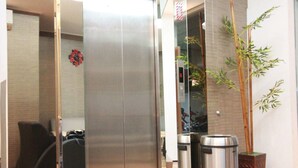 Un ascenseur moderne aux finitions métalliques, un pot de bambou et deux poubelles en acier inoxydable.