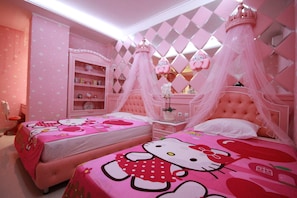 A pink-themed bedroom with two beds, a vanity, and a shelf unit.