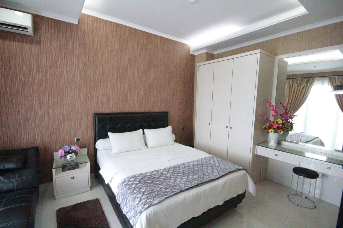 Une chambre d’hôtel comprenant un lit, une table de chevet avec un vase de fleurs, un bureau avec une chaise et une armoire.