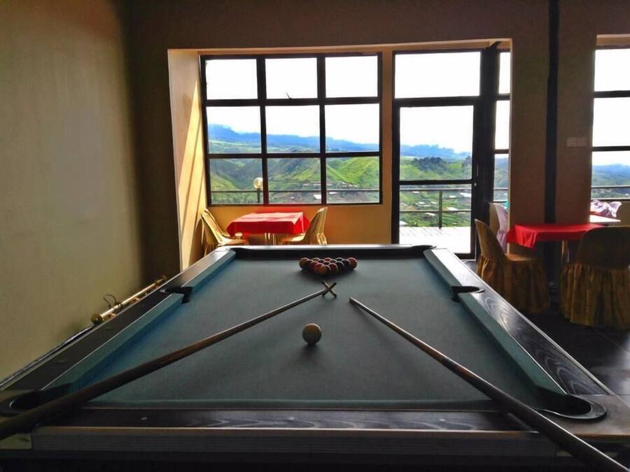 A pool table with a clear view of a mountainous landscape through large windows.