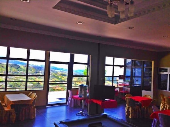 A dining area with tables and chairs, large windows with a view of the countryside, and a ceiling with recessed lighting. - Crystal Hill R (Ranau)