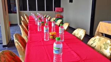 A conference room with a long table covered in a red tablecloth, lined with chairs, and bottles of Dasani water.