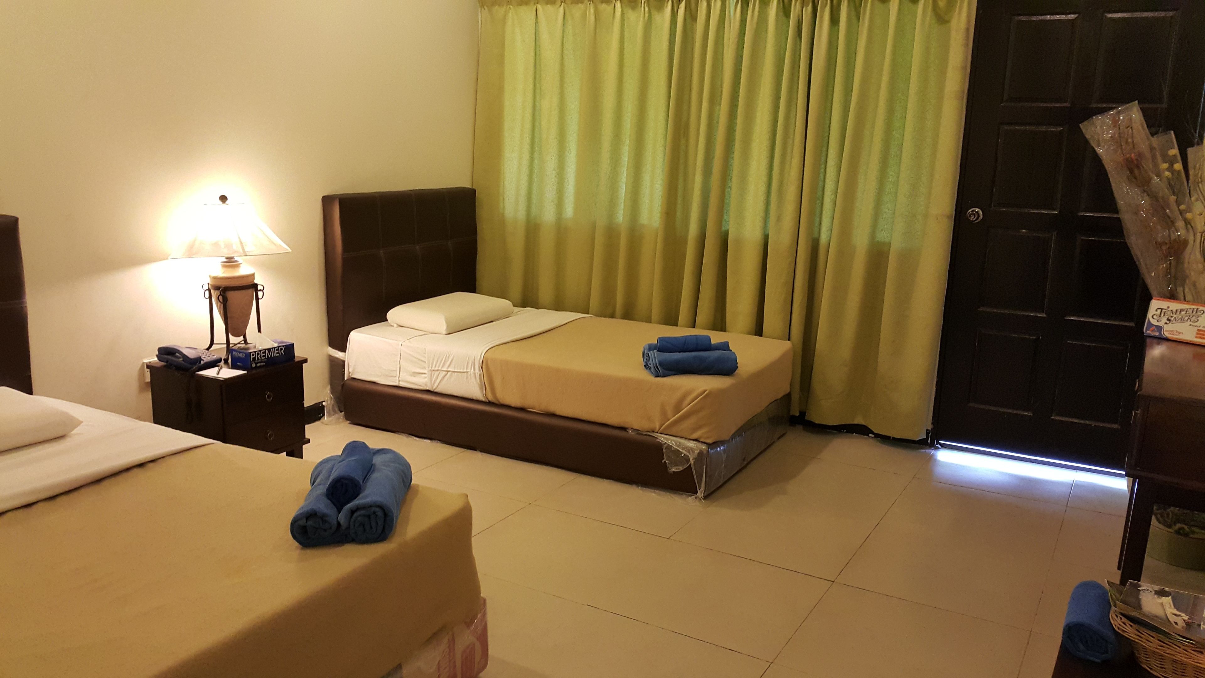 A hotel room with two beds, a nightstand with a lamp, a door, and a window with curtains.