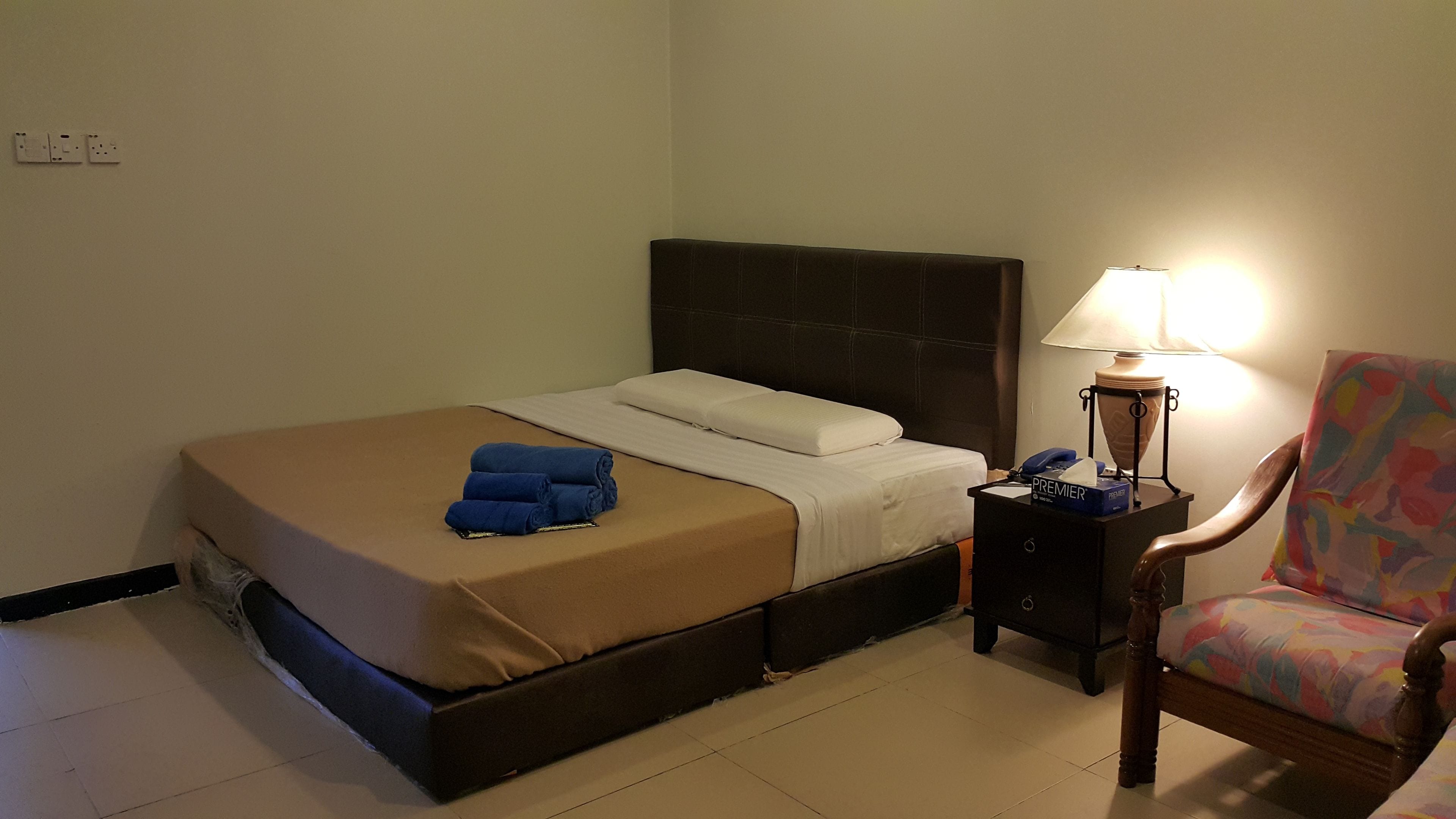 Una habitación de hotel con cama, mesita de noche, lámpara y una silla.
