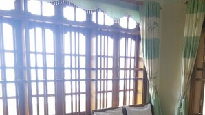 Una habitación con dos camas de madera, una ventana con contraventanas de madera y una cortina.
