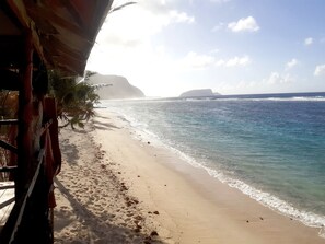 A beach with a wooden structure, clear blue water, and distant rocky formations. - Faofao Beach Fales (Saleapaga)