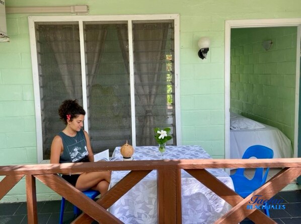 Una habitación con una pared verde, un ventanal con marco blanco, una mesa blanca con un florero y una silla azul.