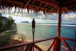 A beach view from a wooden structure with a thatched roof, overlooking the ocean and a distant island. - Faofao Beach Fales (Saleapaga)