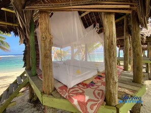 A beach bed with a canopy, wooden pillars, and a view of the ocean. - Faofao Beach Fales (Saleapaga)