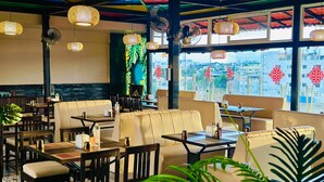 A restaurant with indoor seating, tables, chairs, hanging lights, and large windows with decorative elements. - The Arcadia Coimbatore Airport (Coimbatore)
