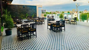 An outdoor seating area with tables and chairs, potted plants, and a patterned floor. - The Arcadia Coimbatore Airport (Coimbatore)