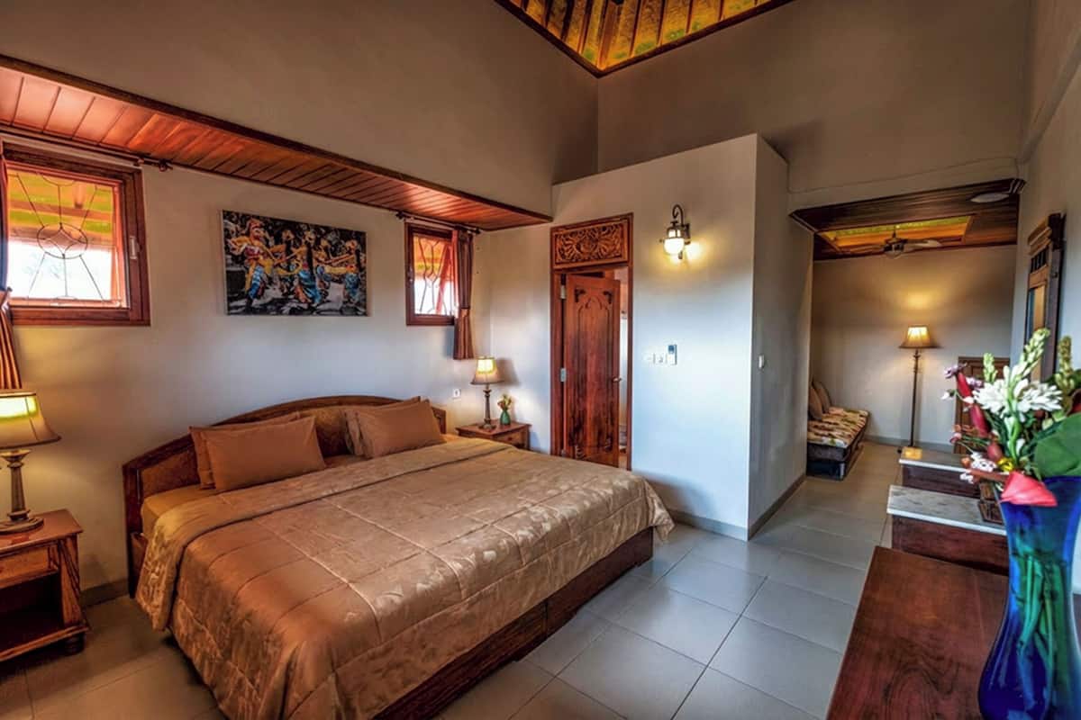 Ein Schlafzimmer mit einem großen Bett, einem Holzkopfteil, zwei Nachttischen mit Lampen, einer Holztür und einem kleinen Tisch mit einer Blumenvase.