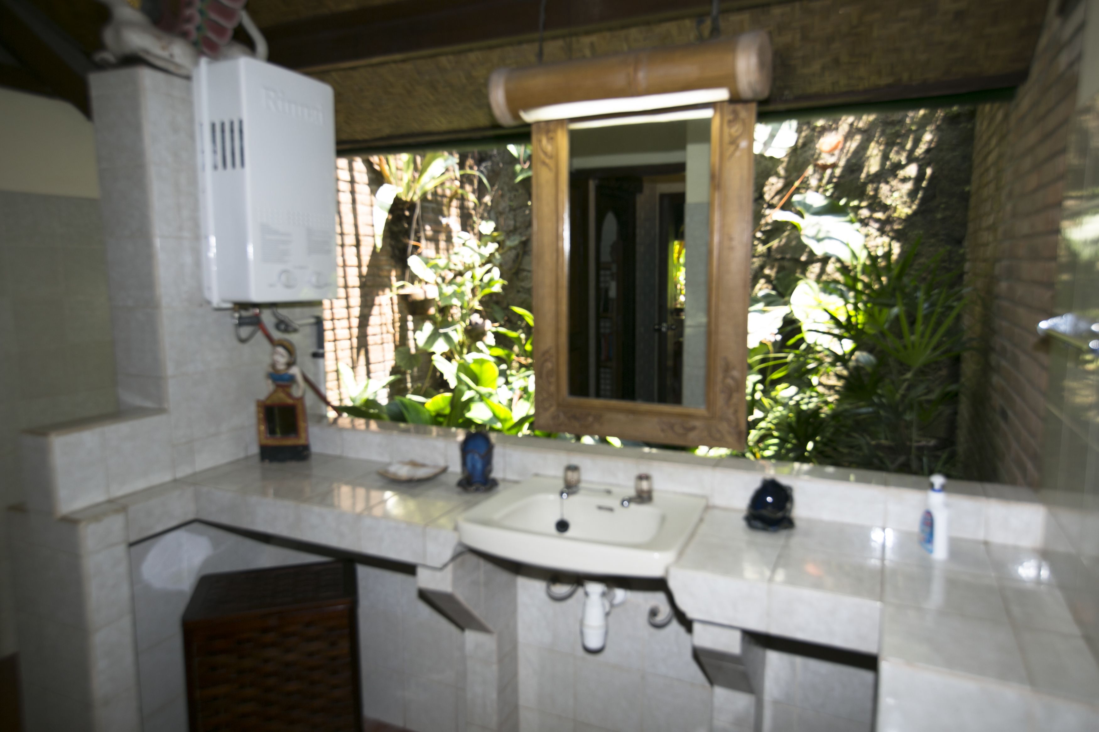 Une salle de bain avec un lavabo, un miroir et une petite fenêtre donnant sur des plantes à l’extérieur.