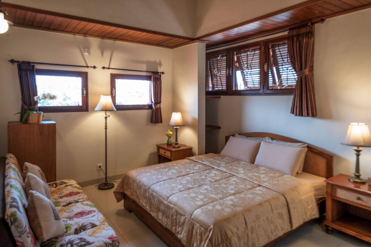 Ein Schlafzimmer mit einem Bett, Nachttischen, einer Couch und zwei mit Vorhängen versehenen Fenstern.