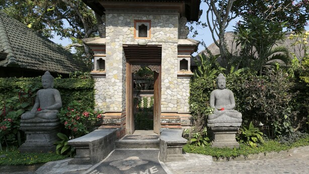 A stone structure with a welcoming sign at the entrance, flanked by two seated Buddha statues. - Murni's Houses and Spa (Ubud)