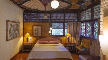 A bedroom with a wooden bed, two bedside tables with lamps, a wicker chair, and a large window with curtains.