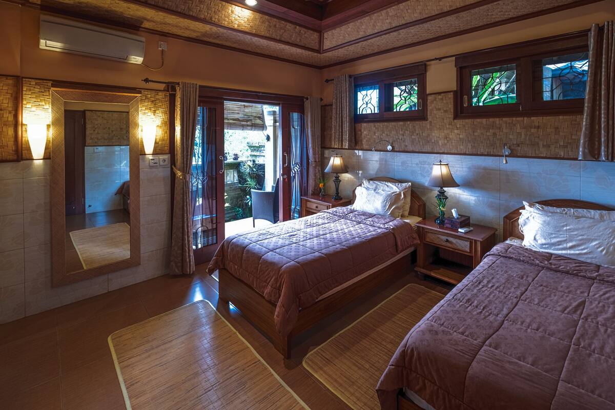 Ein Hotelzimmer mit zwei Betten, einem großen Spiegel und Blick auf den Garten durch die Tür.