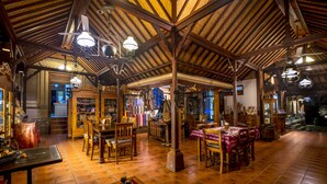 A spacious interior with wooden beams and tiled floors, featuring tables and chairs arranged for dining or socializing. - Murni's Houses and Spa (Ubud)