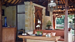 A cozy lounge area with a wooden table, wicker sofa, and potted plants. - Murni's Houses and Spa (Ubud)
