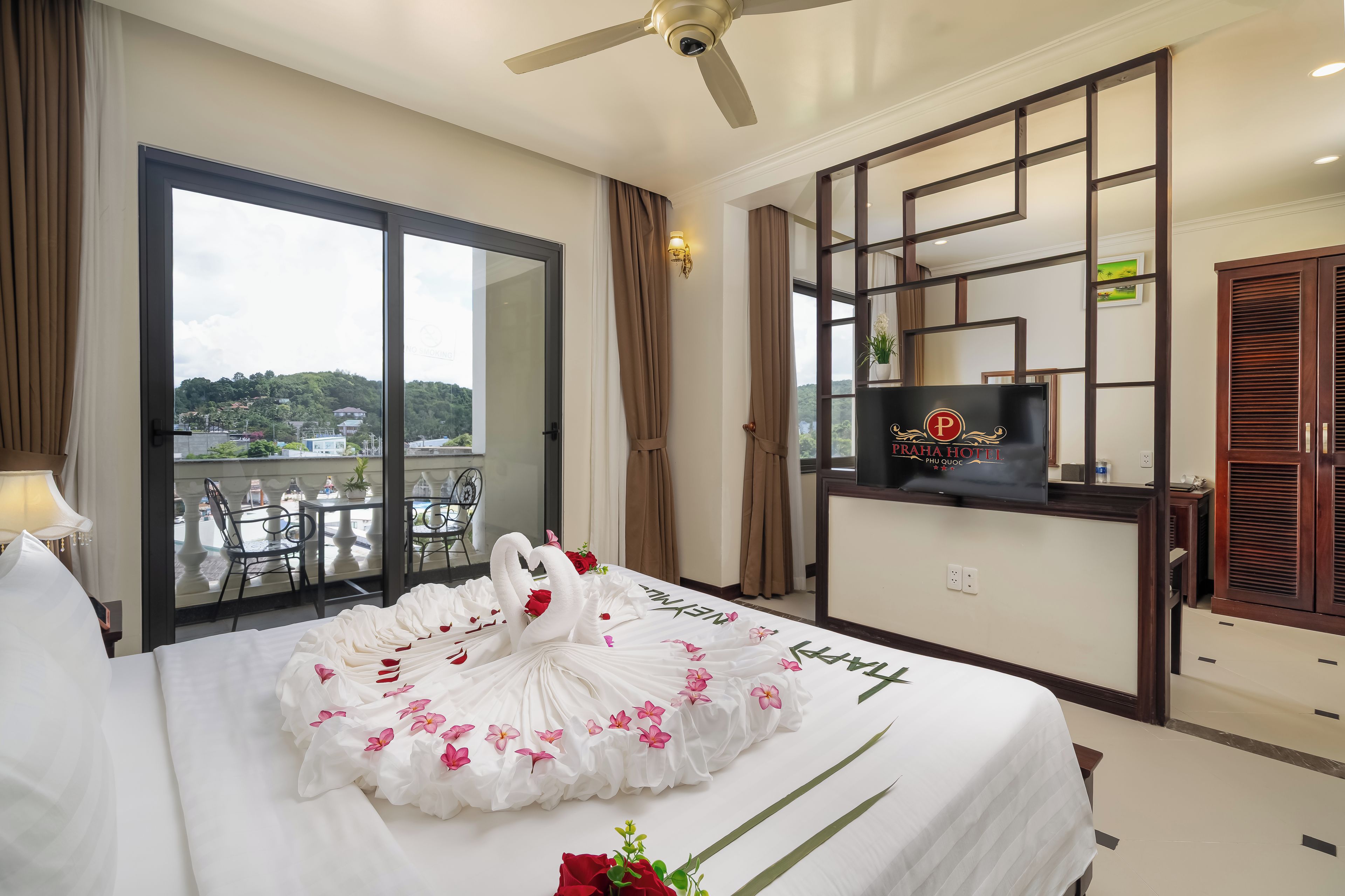 Una habitación de hotel con cama, televisión, balcón con vistas y ventilador de techo.