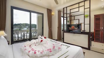 Una habitación de hotel con cama, televisión, balcón con vistas y ventilador de techo.