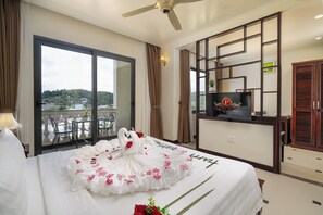 A hotel room with a bed, a television, a balcony with a view, and a ceiling fan.