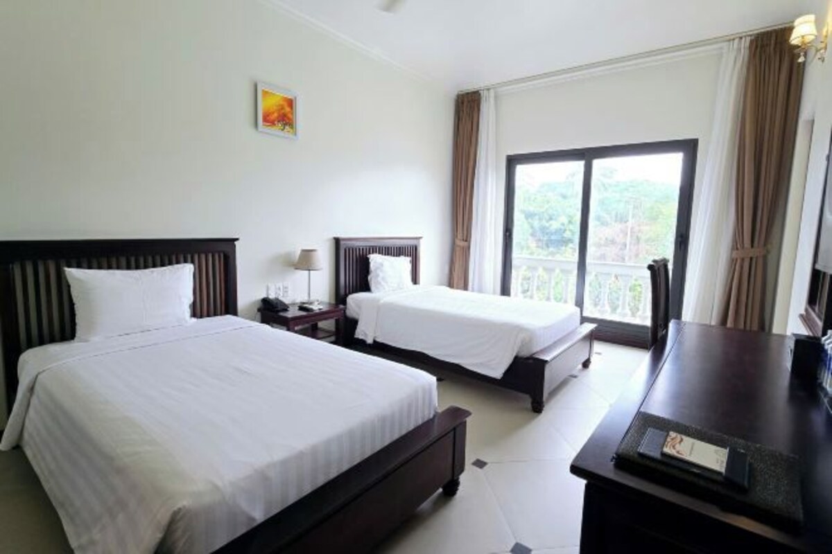 A hotel room with two beds, a desk, and a large window with curtains.