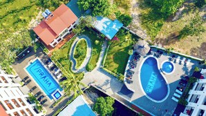 Vista aérea de un complejo turístico con varias piscinas, un jardín central y un edificio con techo rojo.