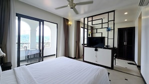 Habitación de hotel con una cama grande, un televisor montado en una mampara negra y un balcón con mesa y sillas.