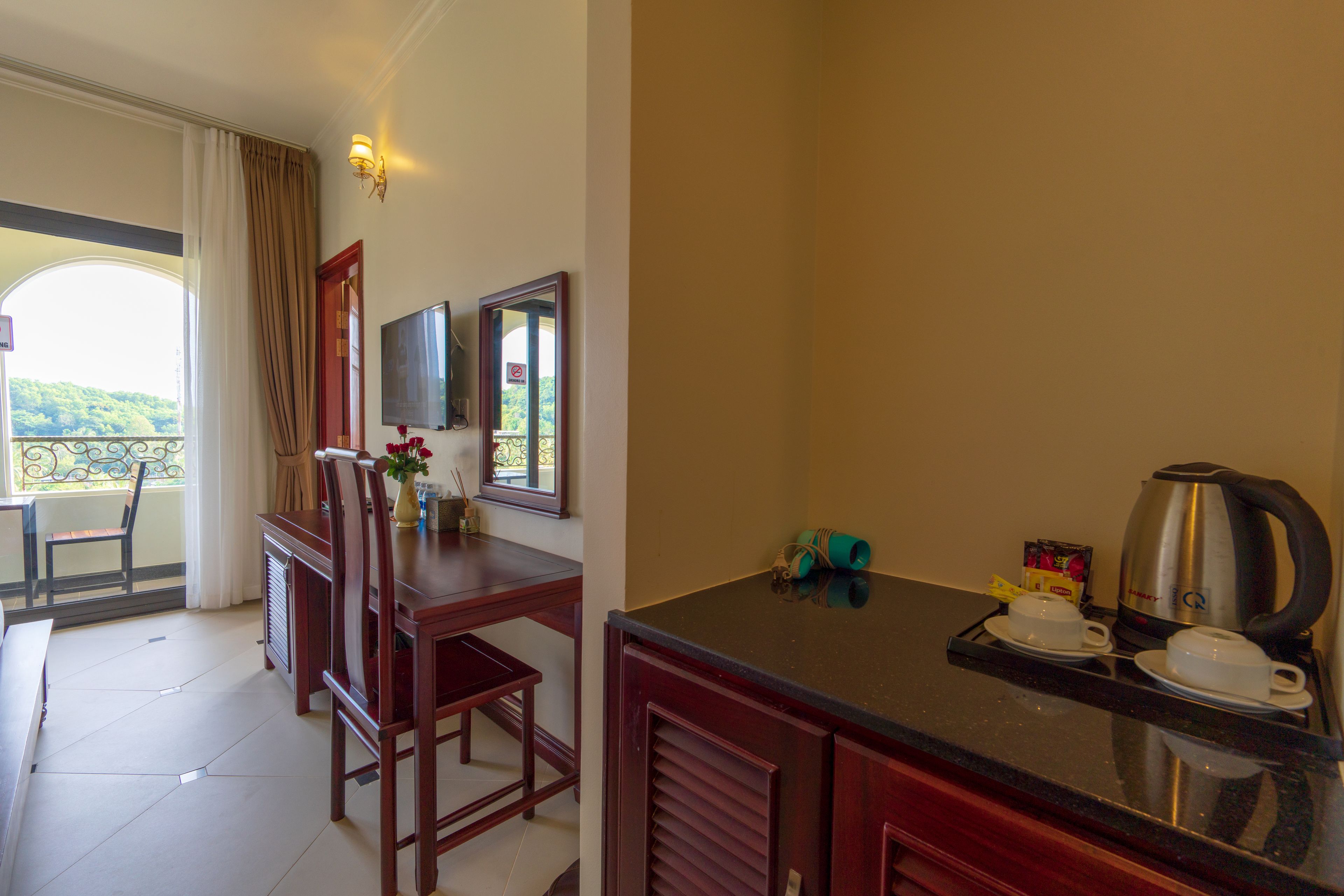 Habitación de hotel con zona de comedor, televisor, ventana con cortinas y kitchenette.