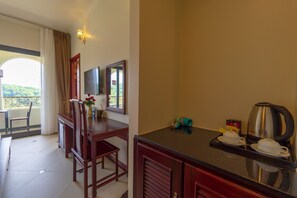 Habitación de hotel con zona de comedor, televisor, ventana con cortinas y kitchenette.