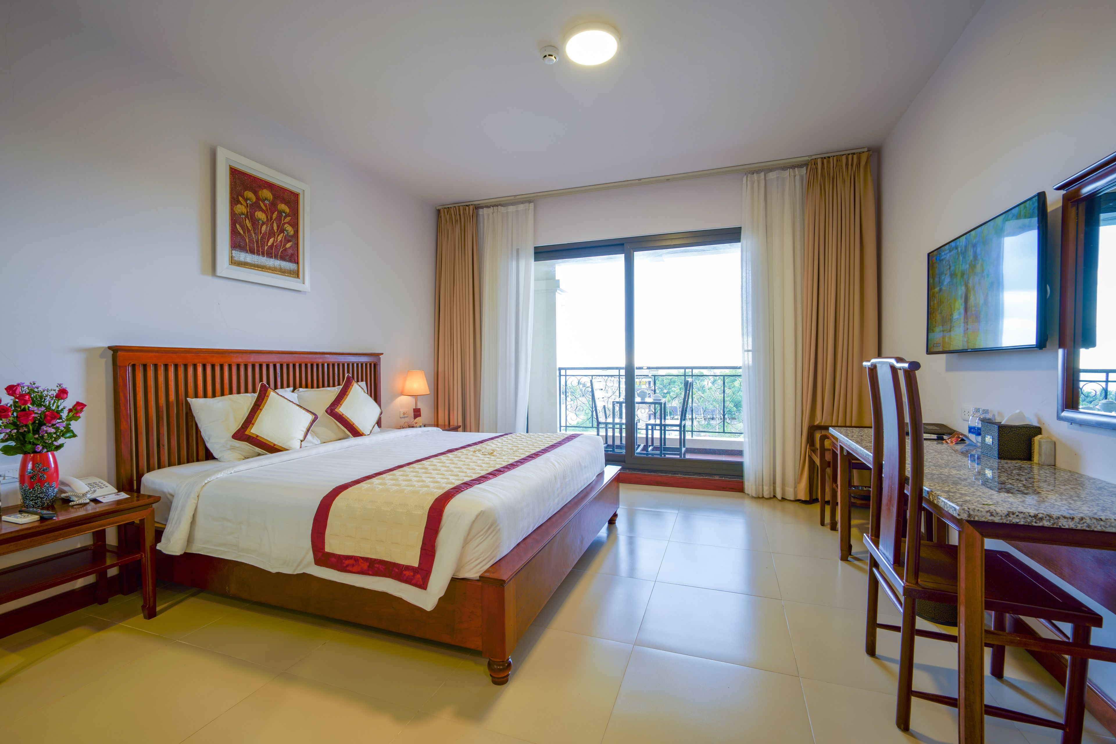A hotel room with a bed, bedside table, lamp, and a view of the outdoors through a balcony.