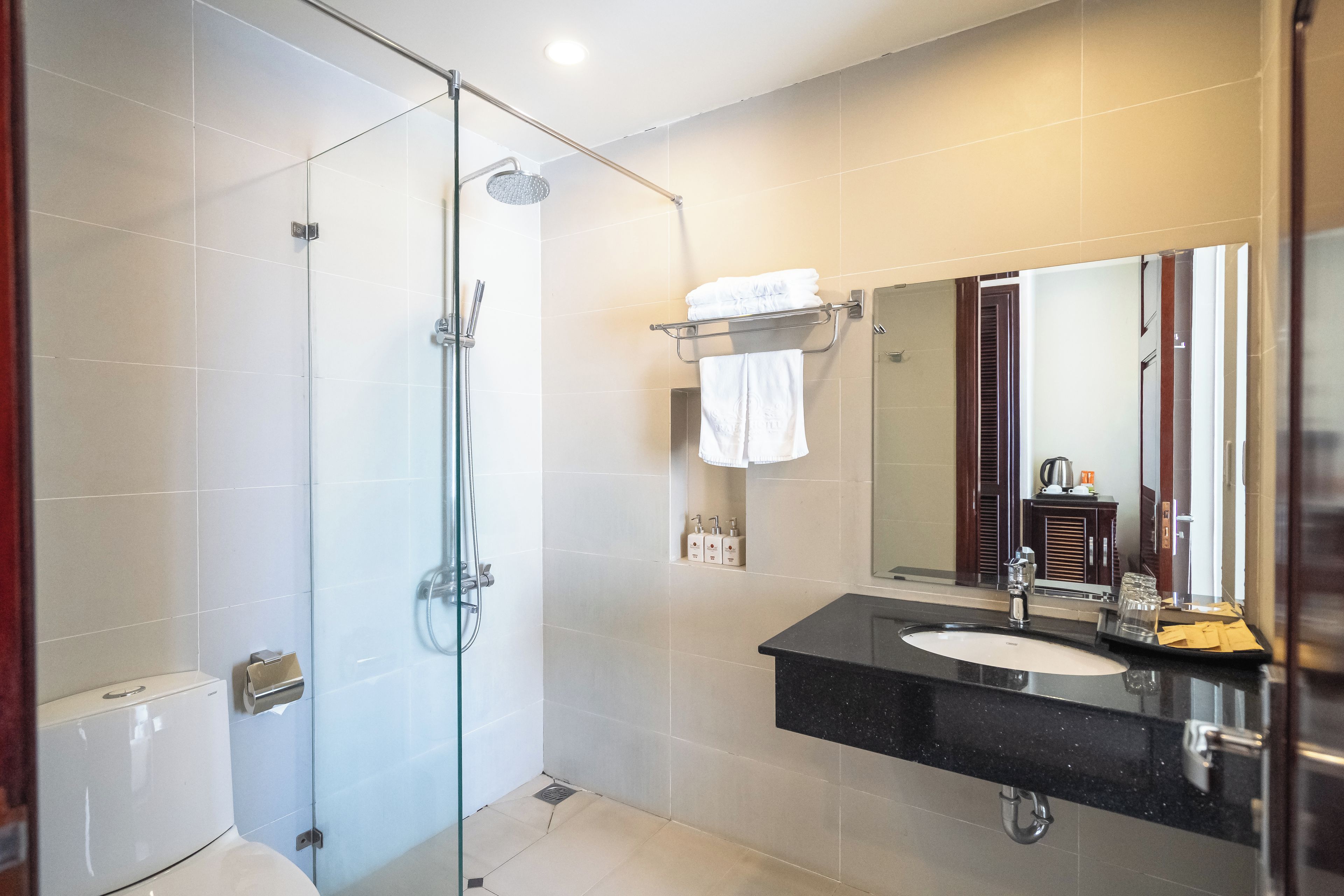 Un baño moderno con ducha envuelta en vidrio, un lavamanos con encimera negra y un espejo grande.