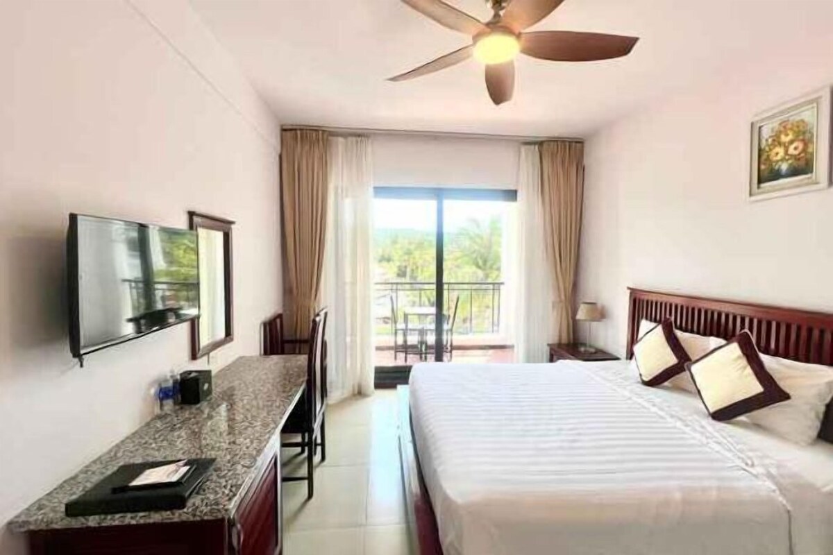 A hotel room with a bed, a desk, a television, and a balcony with curtains.