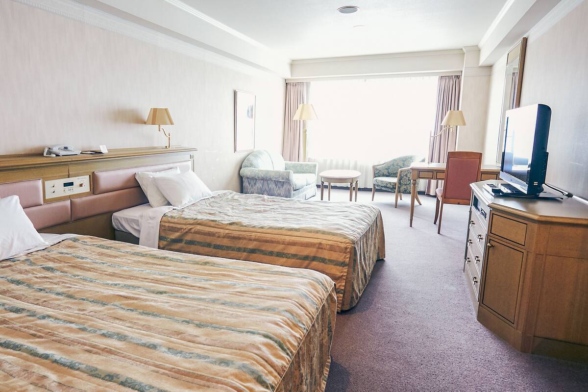 A hotel room with two beds, a desk, a chair, a television, and a window with curtains.