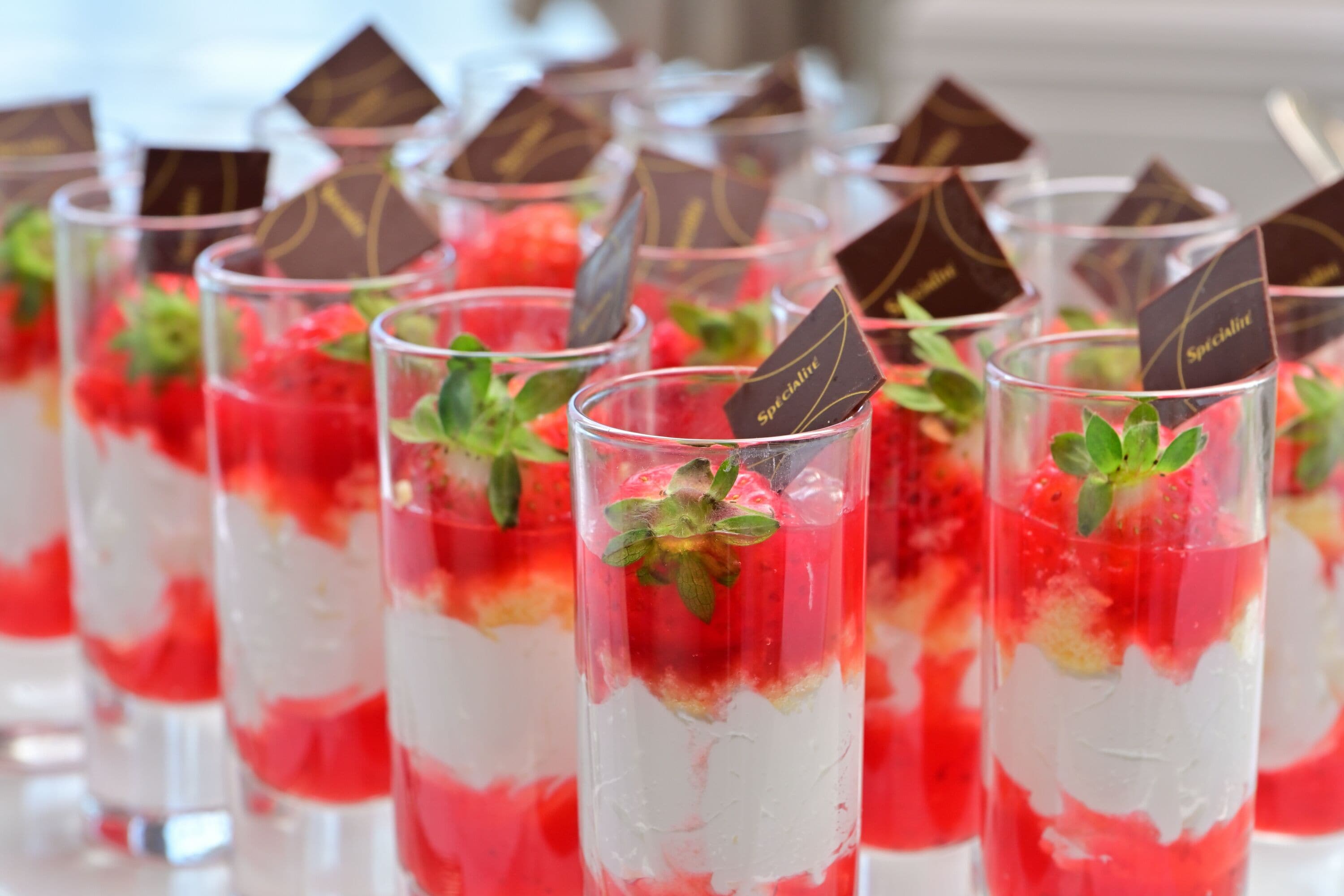 A row of clear glasses filled with layered dessert, garnished with mint leaves and chocolate pieces.