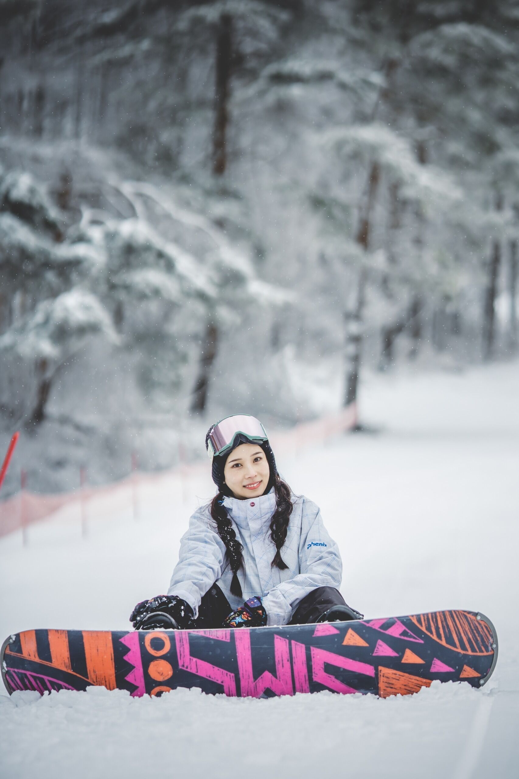 Iemand zit in de sneeuw met een snowboard voor een besneeuwd bos.