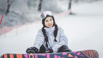 Iemand zit in de sneeuw met een snowboard voor een besneeuwd bos.