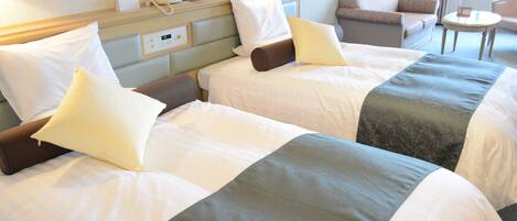 Ein Hotelzimmer mit drei Betten, einem Nachttisch mit Lampe, einem Sessel und einem kleinen Tisch.