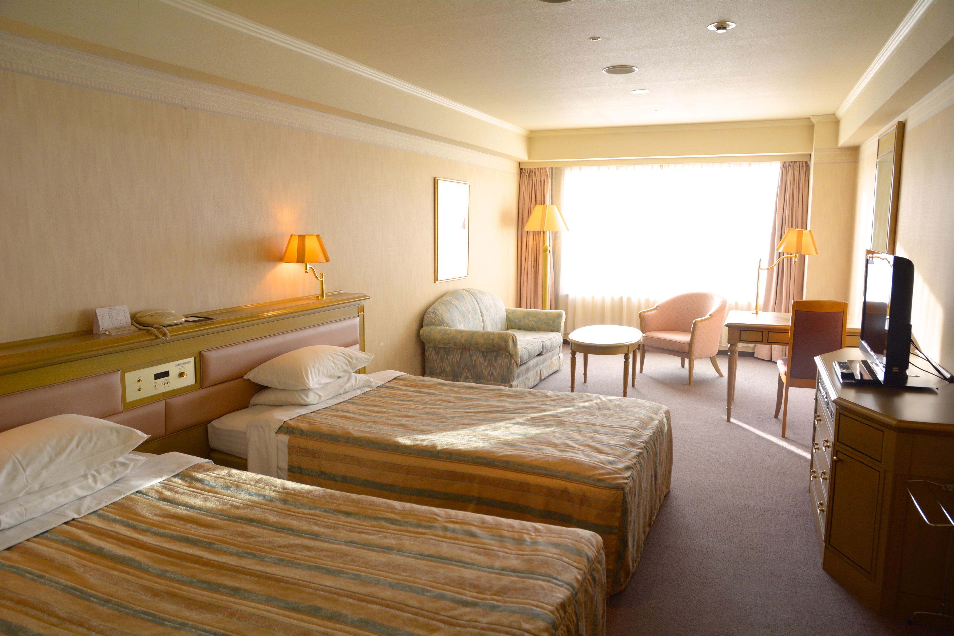 A hotel room with two beds, a desk, a chair, and a television.
