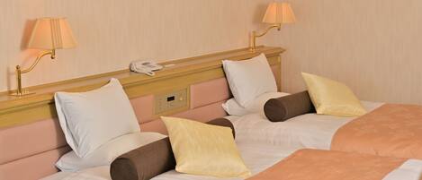 A hotel room with two beds, each with white bedding and multiple pillows. There are two bedside lamps and a phone on the nightstand.