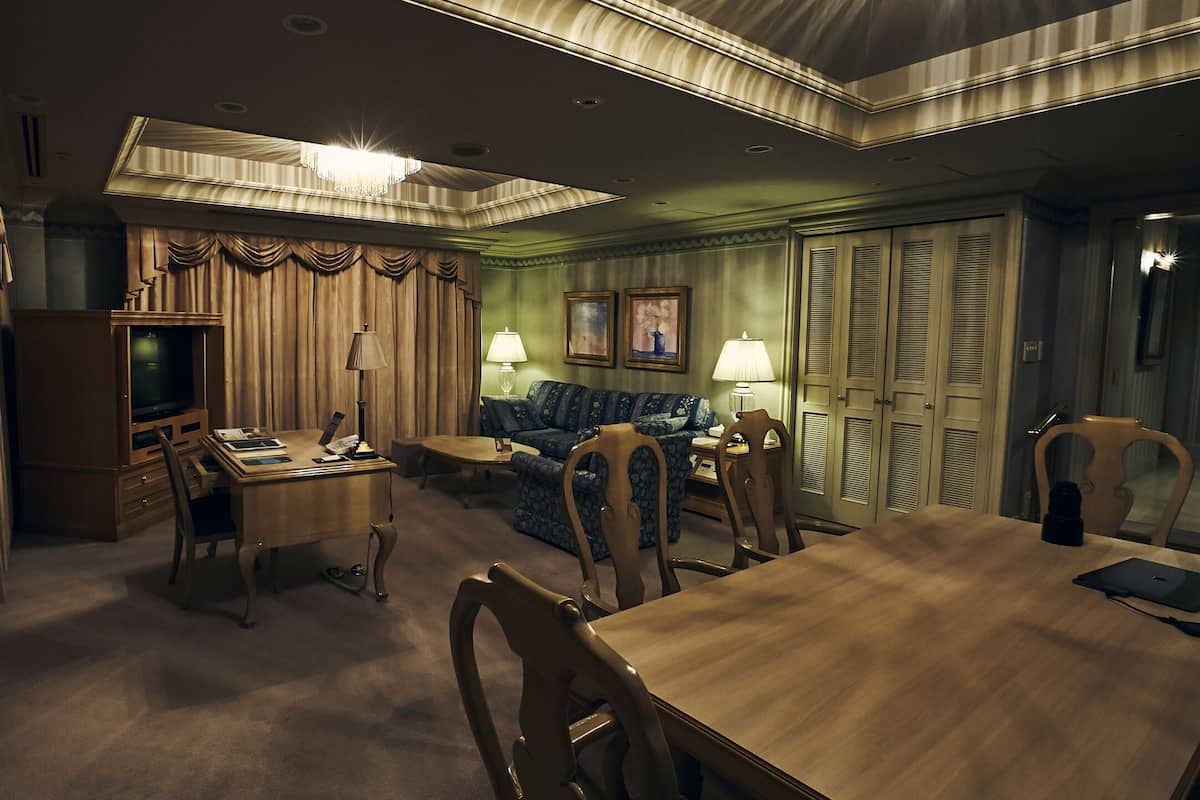 A hotel room with a wooden dining table, two sofas, a television, and a chandelier.