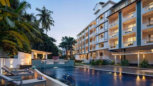 A hotel with a swimming pool, lounge chairs, and a staircase leading to the upper floors. - Ramada by Wyndham Goa Arpora (Arpora)