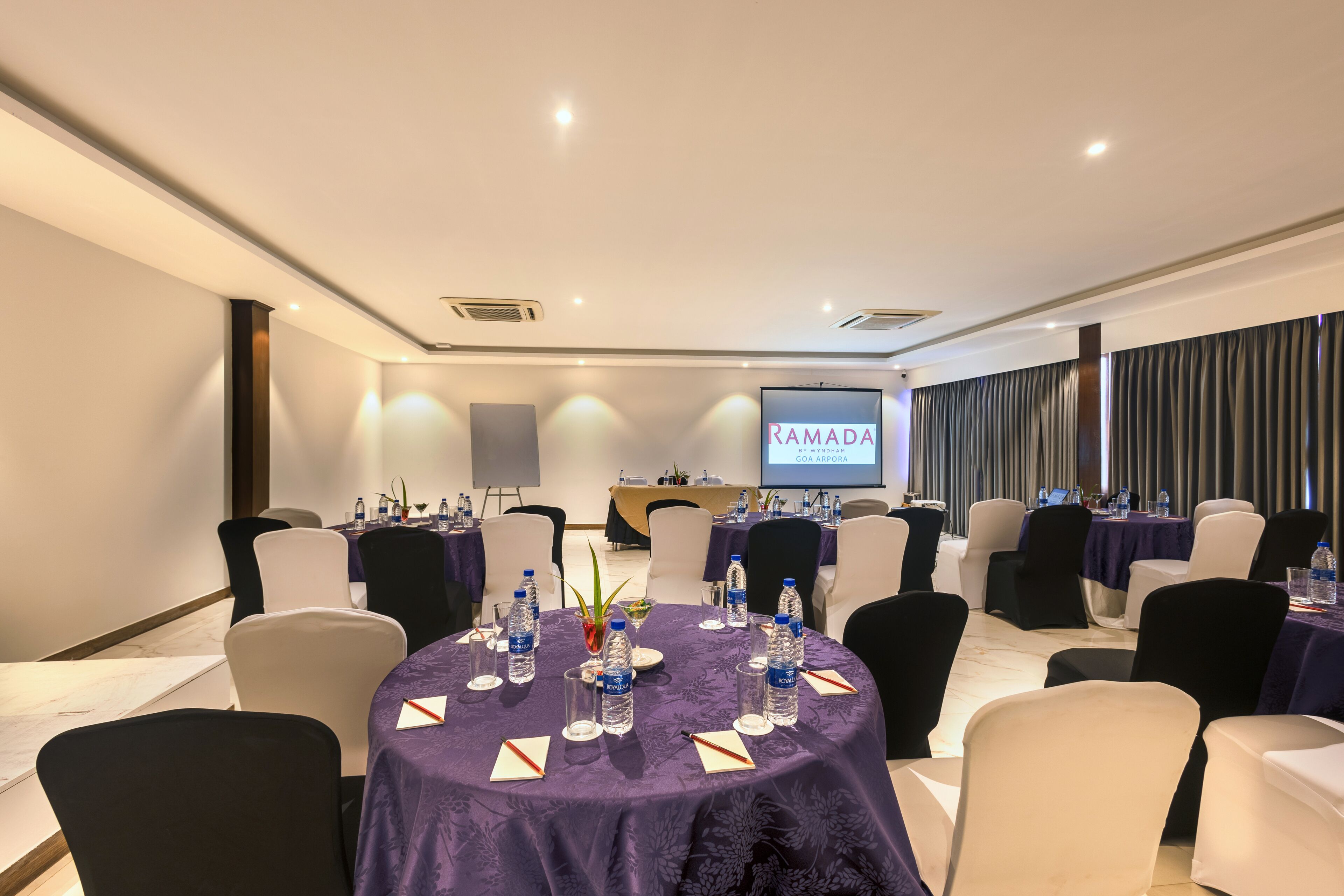 A conference room with round tables, chairs, and a screen displaying "RAMADA".