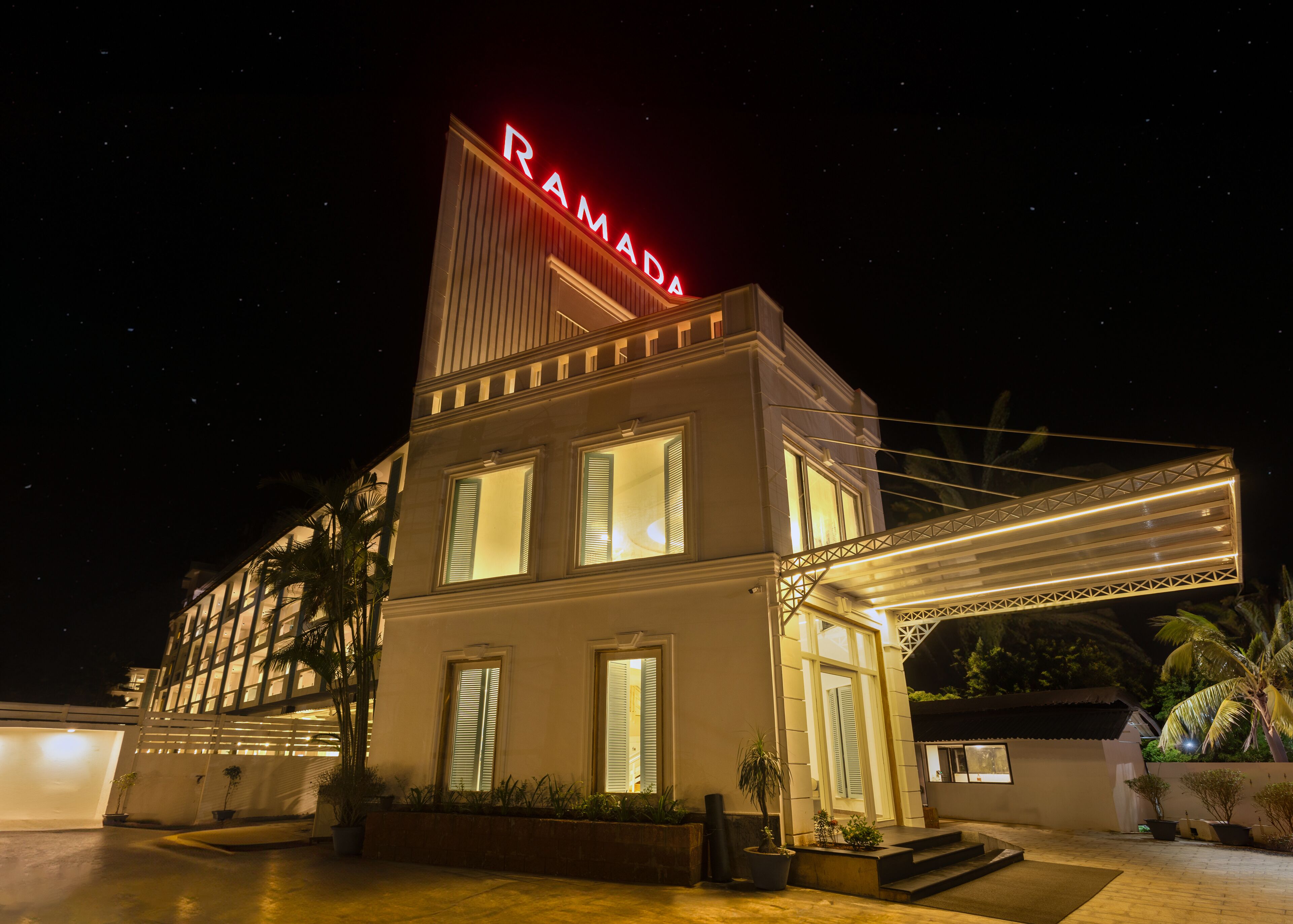 A hotel with a prominent 'RAMADA' sign, a covered entrance, and a well-lit facade.