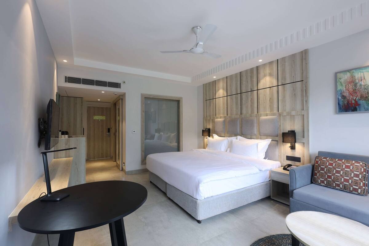 A modern hotel room with a large bed, a sofa, a small table, and a TV.
