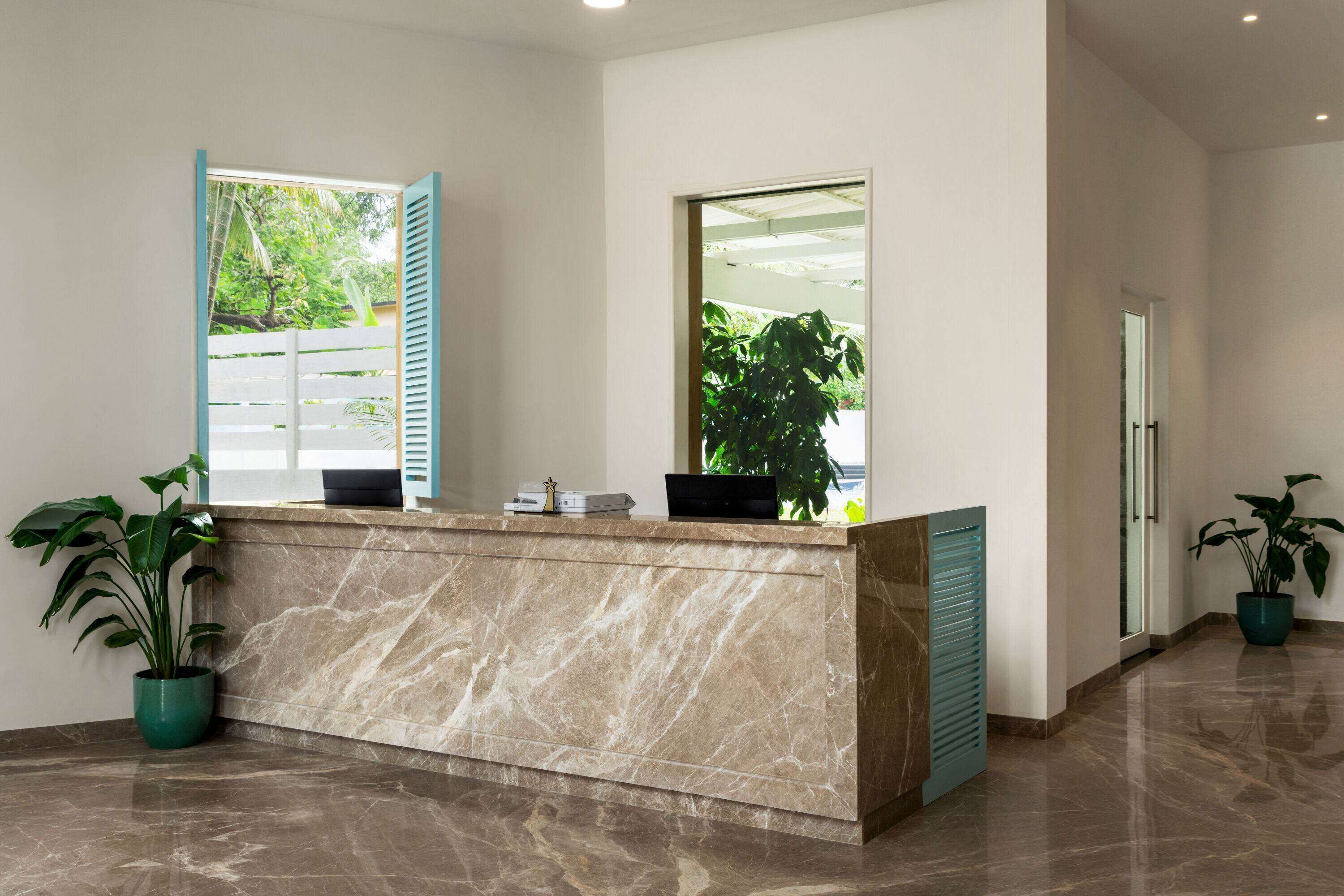 A reception desk with a marble top, two windows with blue shutters, and potted plants.